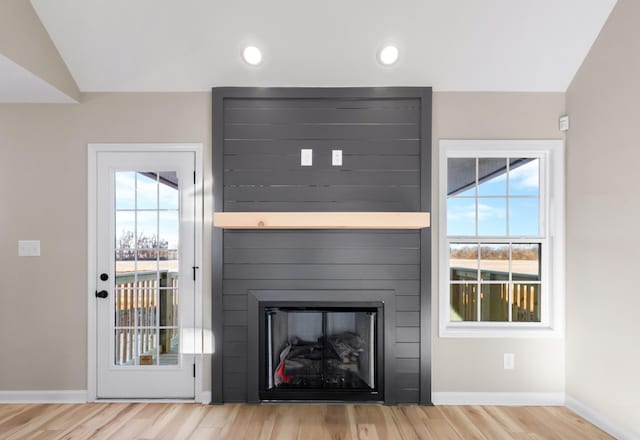 unfurnished living room featuring a large fireplace, a healthy amount of sunlight, baseboards, and wood finished floors