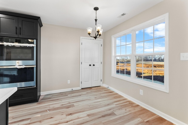 unfurnished dining area featuring light wood-type flooring, baseboards, visible vents, and a chandelier