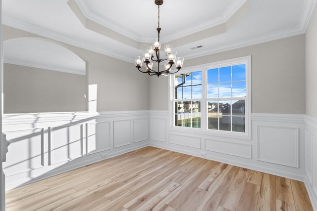 unfurnished dining area with visible vents, a raised ceiling, wainscoting, crown molding, and light wood-style floors