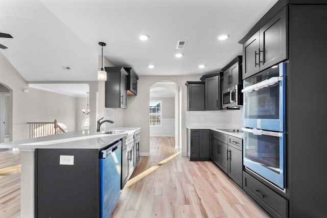 kitchen with arched walkways, stainless steel appliances, light countertops, a sink, and light wood-type flooring