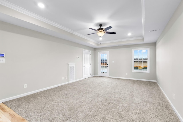 carpeted empty room featuring a raised ceiling, visible vents, ornamental molding, ceiling fan, and baseboards