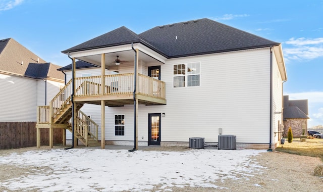 snow covered rear of property featuring a shingled roof, a ceiling fan, stairway, fence, and central AC