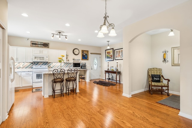 kitchen with white appliances, light hardwood / wood-style flooring, backsplash, hanging light fixtures, and white cabinets