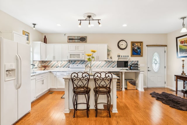 kitchen featuring a kitchen breakfast bar, white appliances, light hardwood / wood-style flooring, backsplash, and a center island