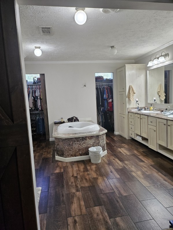 bathroom featuring crown molding, vanity, a textured ceiling, wood-type flooring, and a bathtub