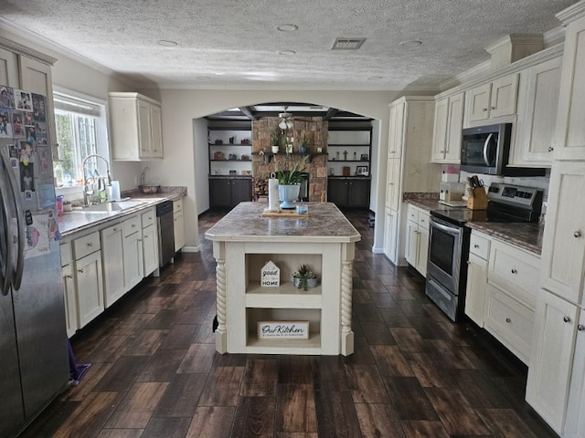 kitchen with a textured ceiling, a kitchen island, appliances with stainless steel finishes, dark wood-type flooring, and sink