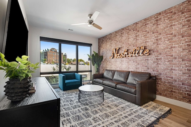 living room featuring ceiling fan, wood-type flooring, and brick wall