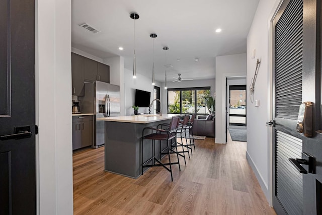 kitchen with light wood-type flooring, ceiling fan, stainless steel fridge with ice dispenser, a breakfast bar area, and a center island with sink