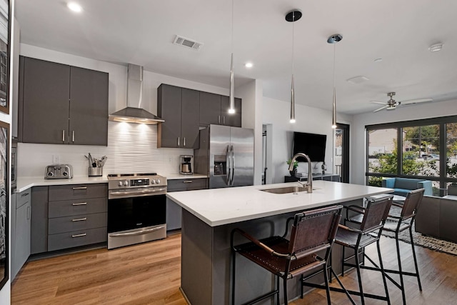 kitchen featuring backsplash, light hardwood / wood-style flooring, appliances with stainless steel finishes, wall chimney exhaust hood, and ceiling fan