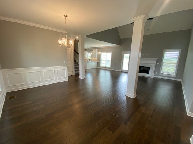 unfurnished living room with a notable chandelier, crown molding, dark hardwood / wood-style flooring, vaulted ceiling, and ornate columns