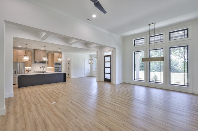 unfurnished living room featuring coffered ceiling, crown molding, sink, beam ceiling, and light hardwood / wood-style floors