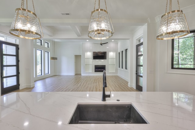 kitchen featuring a fireplace, light stone countertops, light hardwood / wood-style floors, sink, and beam ceiling