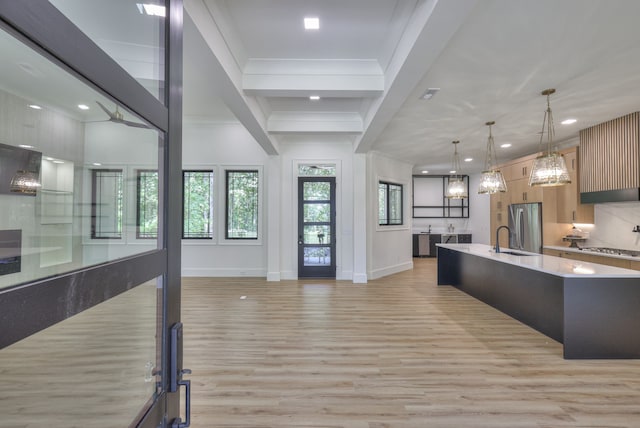 kitchen featuring an island with sink, hanging light fixtures, stainless steel refrigerator, sink, and light wood-type flooring