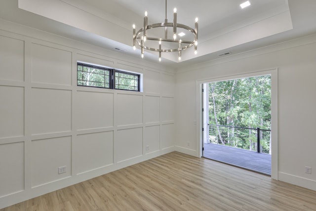 unfurnished room featuring light wood-type flooring, a raised ceiling, and an inviting chandelier