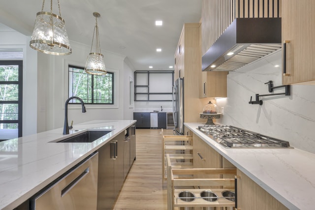 kitchen featuring light wood-type flooring, backsplash, light stone counters, appliances with stainless steel finishes, and wall chimney range hood