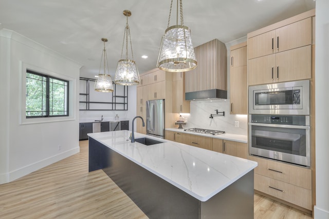 kitchen with a kitchen island with sink, appliances with stainless steel finishes, light wood-type flooring, and decorative backsplash