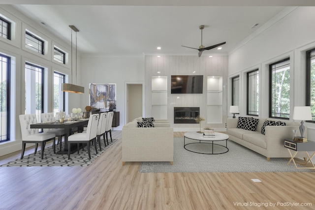 living room with ornamental molding, ceiling fan, a large fireplace, and light hardwood / wood-style floors