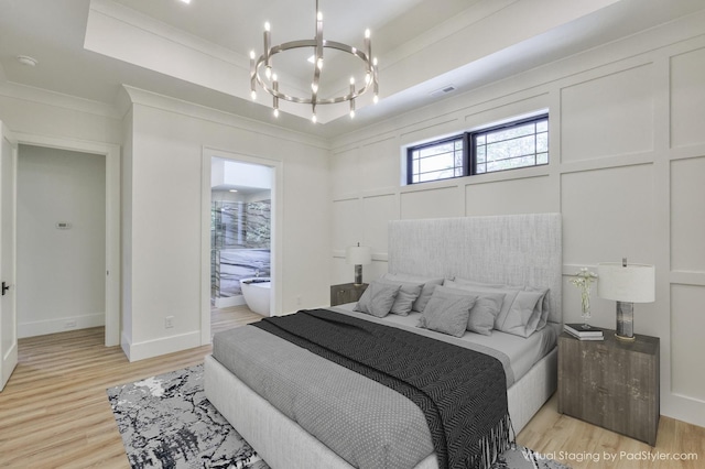 bedroom with ensuite bathroom, light hardwood / wood-style flooring, a notable chandelier, a raised ceiling, and ornamental molding