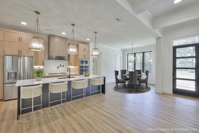 kitchen with a center island with sink, a kitchen breakfast bar, appliances with stainless steel finishes, and wall chimney exhaust hood