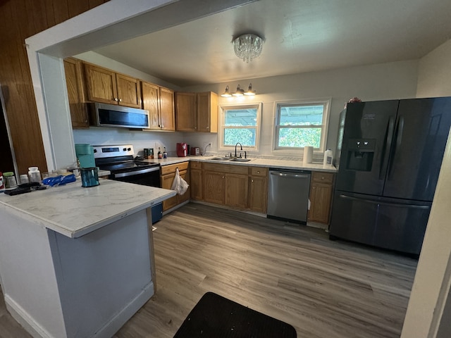 kitchen with light stone counters, stainless steel appliances, light hardwood / wood-style floors, sink, and kitchen peninsula