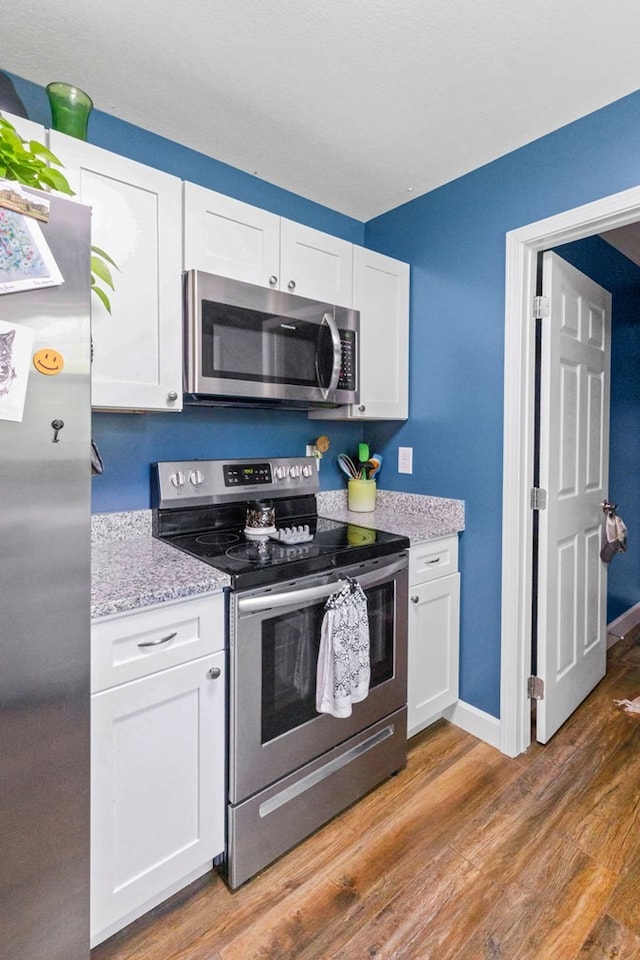 kitchen with hardwood / wood-style floors, appliances with stainless steel finishes, white cabinets, and light stone countertops