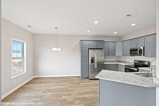 kitchen with gray cabinetry, sink, hanging light fixtures, light stone countertops, and stainless steel appliances