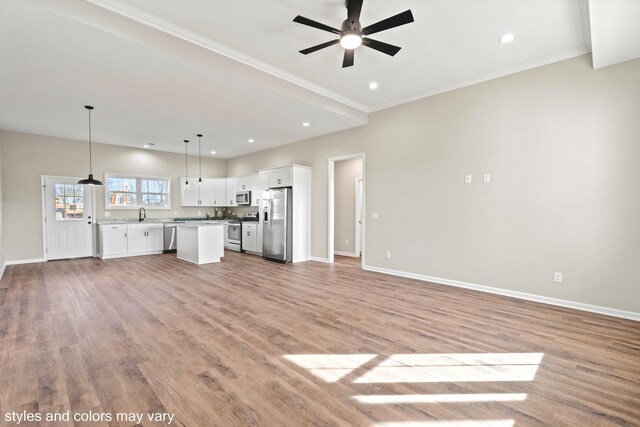 unfurnished living room with ceiling fan, sink, ornamental molding, and light wood-type flooring