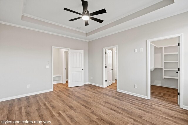 unfurnished bedroom with light wood-type flooring, a walk in closet, a raised ceiling, ceiling fan, and a closet