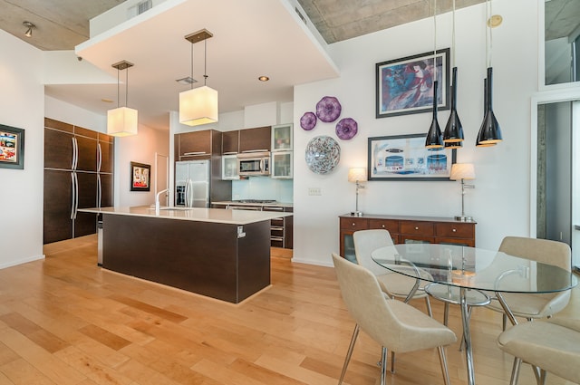 kitchen featuring dark brown cabinets, light hardwood / wood-style flooring, hanging light fixtures, appliances with stainless steel finishes, and a center island with sink