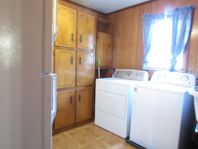 clothes washing area with cabinet space, wooden walls, and separate washer and dryer