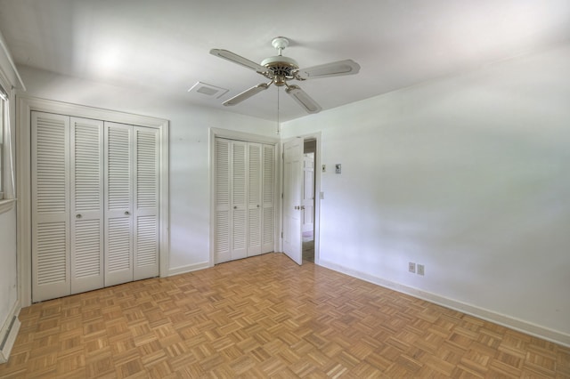 unfurnished bedroom with two closets, ceiling fan, and light parquet floors