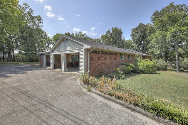 view of side of property featuring a garage, brick siding, a yard, and driveway