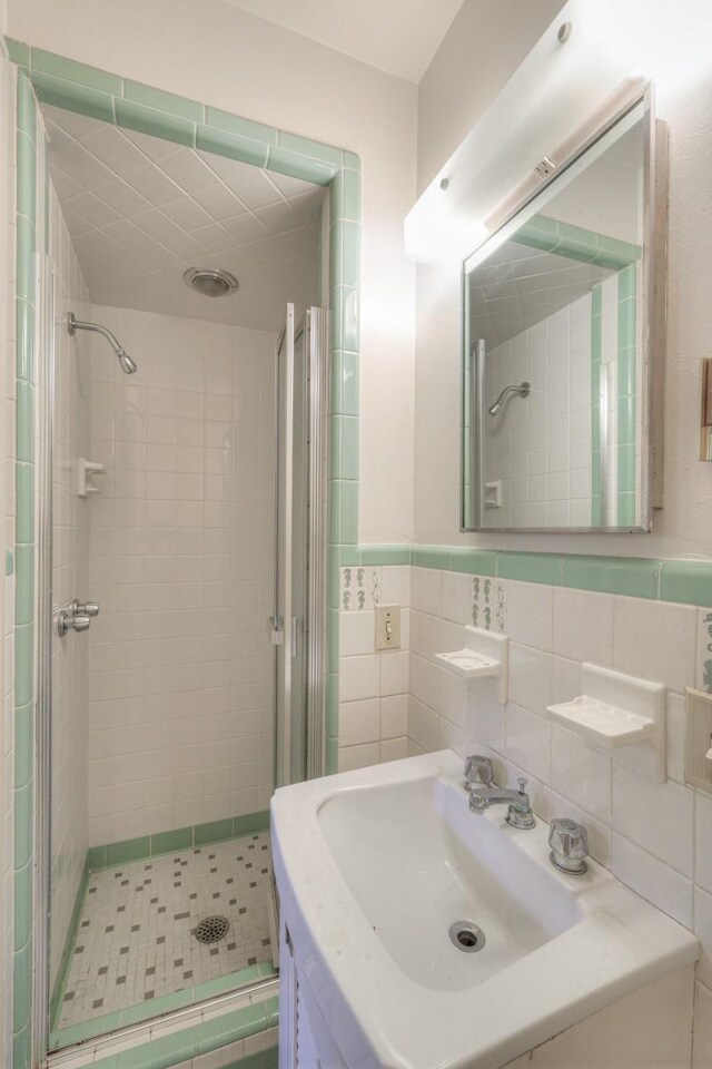 bathroom with a stall shower, wainscoting, a sink, and tile walls