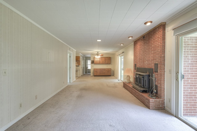 unfurnished living room with a wealth of natural light, light colored carpet, a wood stove, and ornamental molding