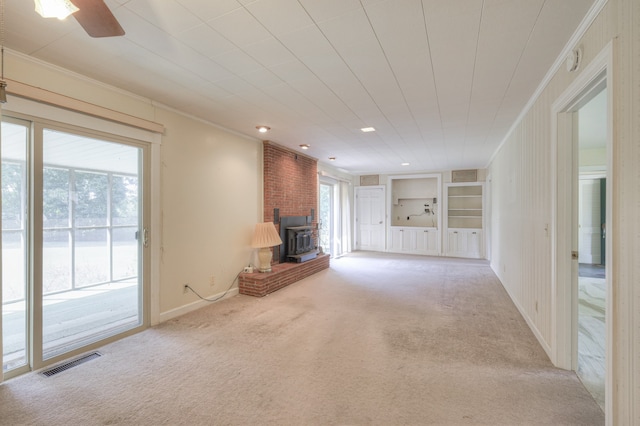 unfurnished living room with light colored carpet, a healthy amount of sunlight, and a wood stove