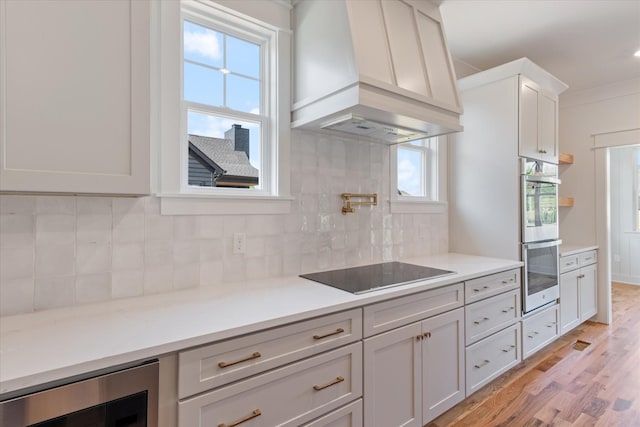 6816 Springwater St, Smyrna, TN 37167 - kitchen with premium range hood, black electric stovetop, stainless steel double oven, wine cooler, and light wood-style flooring