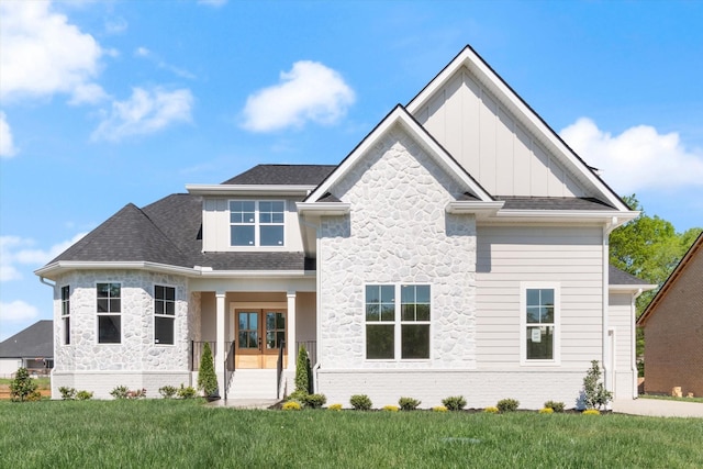 view of front of home with stone siding, roof with shingles, french doors, a front lawn, and board and batten siding