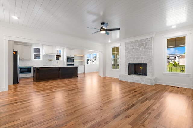 6816 Springwater St, Smyrna, TN 37167 - unfurnished living room featuring ceiling fan, light wood-style flooring, a stone fireplace, a sink, and baseboards