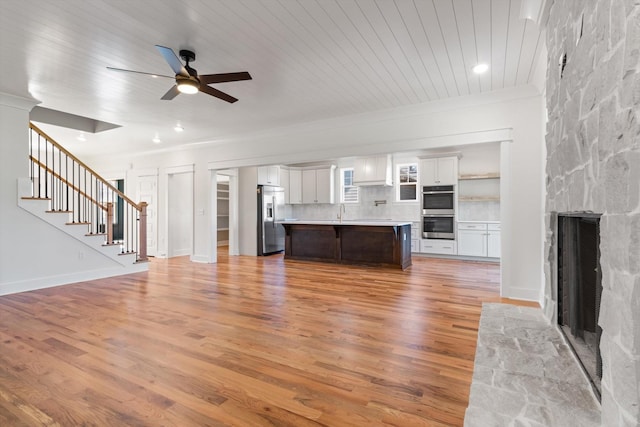 6816 Springwater St, Smyrna, TN 37167 - unfurnished living room with a stone fireplace, a ceiling fan, light wood-type flooring, stairway, and crown molding