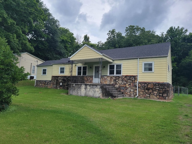 ranch-style house featuring a porch, stone siding, a shingled roof, and a front lawn