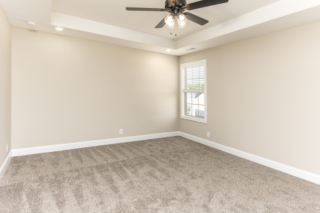 carpeted spare room with ceiling fan and a raised ceiling