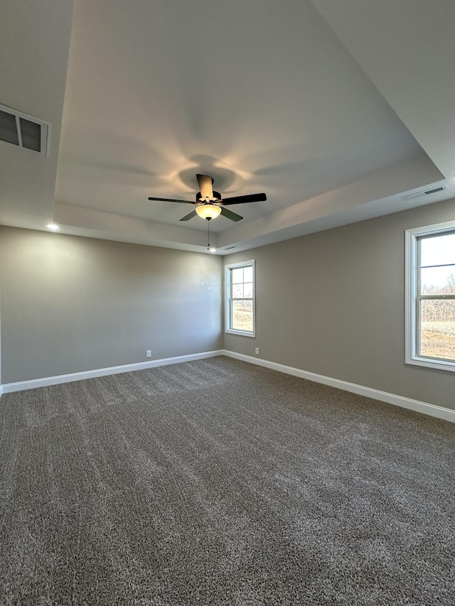 unfurnished room featuring a raised ceiling, ceiling fan, and dark carpet