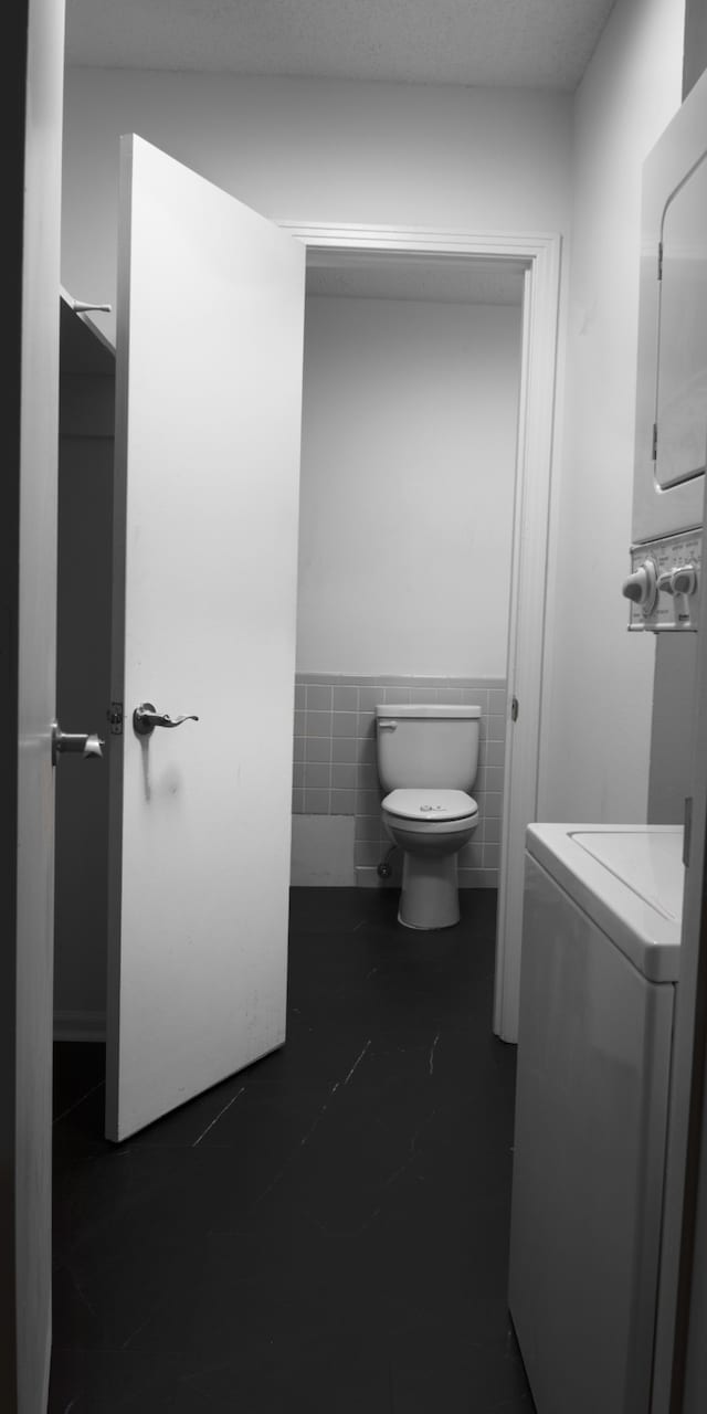 bathroom featuring tile patterned flooring, tile walls, toilet, and stacked washer / drying machine