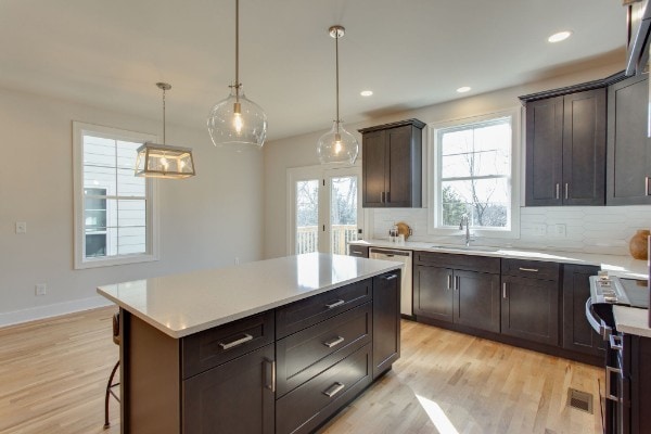 kitchen with a kitchen island, backsplash, appliances with stainless steel finishes, sink, and light wood-type flooring