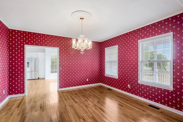 unfurnished dining area with a wealth of natural light, ornamental molding, a notable chandelier, and light hardwood / wood-style flooring