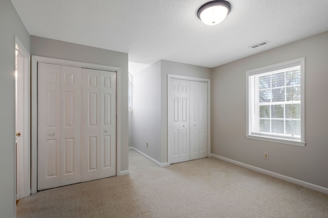 unfurnished bedroom with a textured ceiling, light carpet, and multiple closets