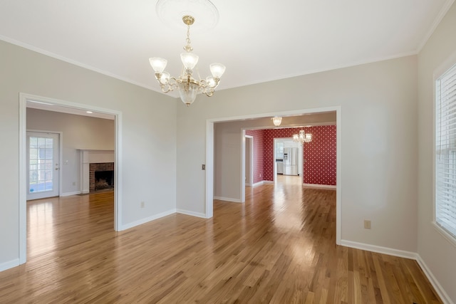 spare room with ornamental molding, light hardwood / wood-style flooring, a notable chandelier, and a fireplace