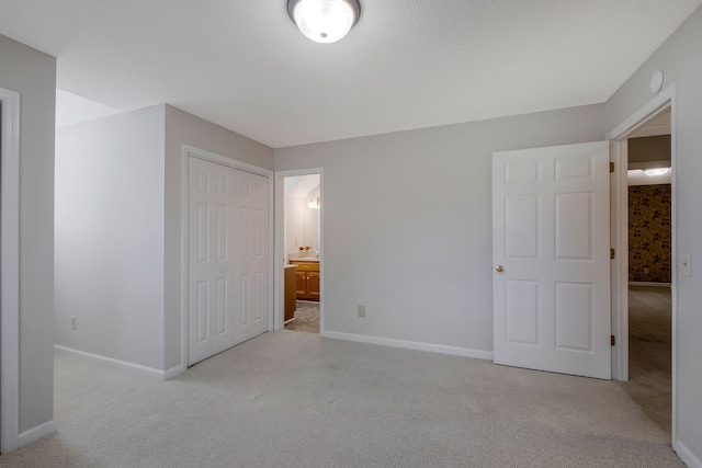 unfurnished bedroom featuring ensuite bath, light colored carpet, and a closet