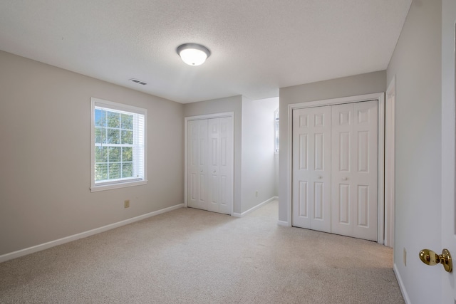 unfurnished bedroom featuring a textured ceiling, light colored carpet, and multiple closets