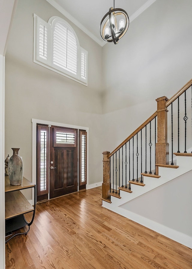 entrance foyer with a high ceiling, hardwood / wood-style flooring, a notable chandelier, and ornamental molding